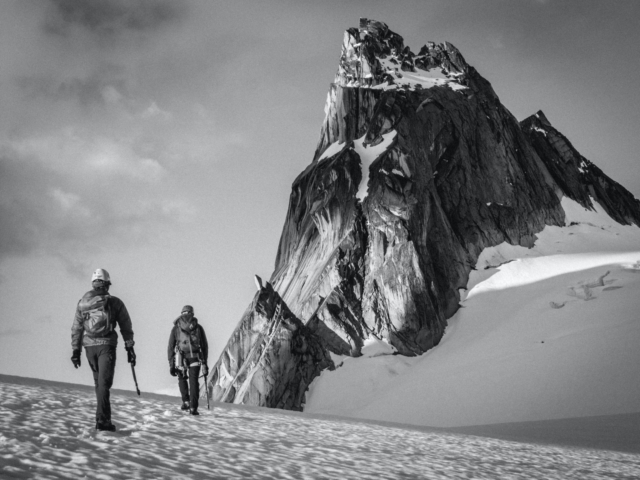 Two mountaineers on a glacier below a rocky peak